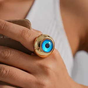 Macro detail of a chunky gold ring featuring a blue resin evil eye design on a hand