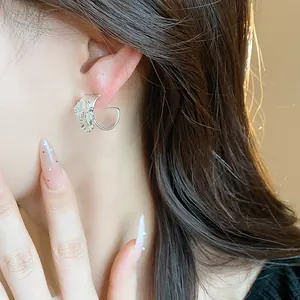 Vista detallada de pendiente de flor en plata mate con forma de C en la oreja del modelo