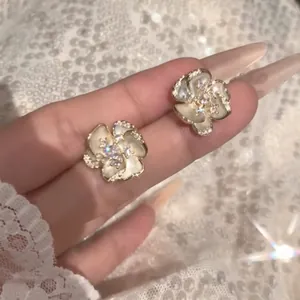 Close-up of elegant white camellia earrings with sparkling rhinestones in gold tone.