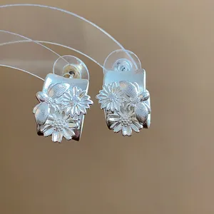 Detalle de pendientes de botón en C plata mate con motivos de flores y abejas.