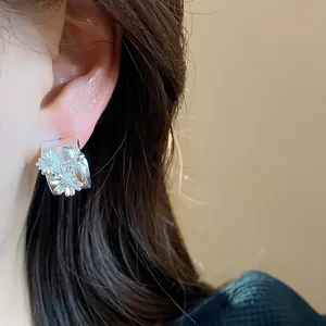 Primer plano de un pendiente de aro en C con flor de plata mate usado en la oreja, elegante