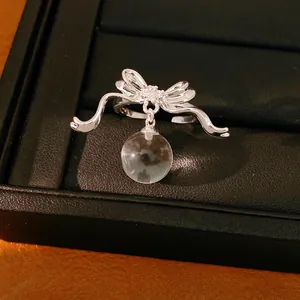 Macro view of a silver bow ring with zircon accents and a dangling clear resin sphere.