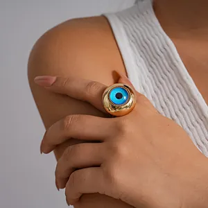 Detailed view of a chunky gold-tone ring featuring a large blue resin evil eye motif