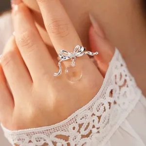 Detailed view of elegant silver bow ring with clear resin bead charm worn on finger