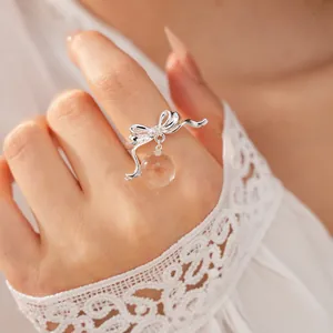 Detailed macro view of a silver-toned bow ring with a dangling clear resin bead on a finger