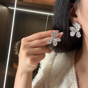 Exquisite detail of luxury zircon-encrusted flower stud earrings on an ear and hand.