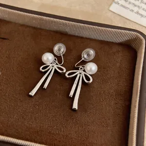 Detailed close-up of silver bow clip-on earrings with elegant white pearl accents