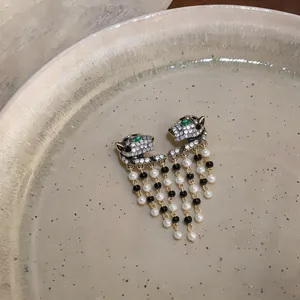 Detailed macro view of luxurious leopard head earrings with dangling pearl and black bead tassels