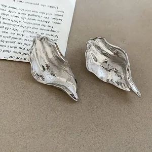 Detailed close-up of irregular silver leaf earrings with metallic crumpled texture
