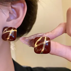 Close-up of deep red enamel square stud earrings with golden cross pattern and silver needles.