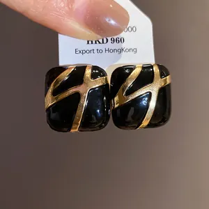 Detailed macro view of square black enamel earrings with golden geometric design patterns