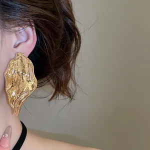 Close-up of a statement gold leaf earring with irregular texture on an Asian model's ear