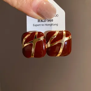 Detailed macro view of square red enamel stud earrings featuring elegant golden cross patterns