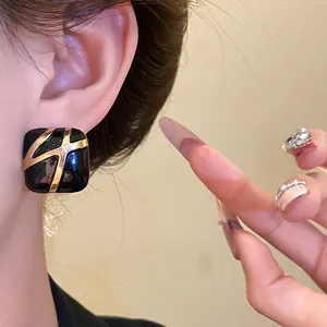 Close-up view showing the textured detail of a black and gold enamel square earring