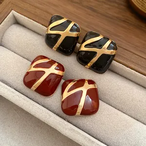 Macro detail view of square enamel stud earrings in black and red with gold patterns