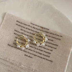 Close-up of French style gold hoop earrings with white pearl flowers on a linen background.