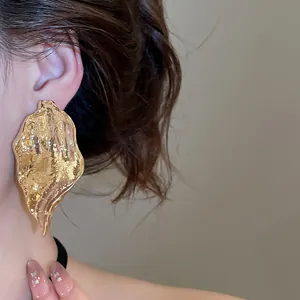 Close-up of large golden irregular leaf earring with metallic pleated texture