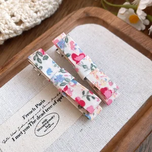 Macro detail showing the floral fabric texture of two sweet bow-shaped duckbill hair clips.