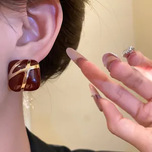 Close-up of elegant burgundy square stud earrings with gold cross pattern on ear