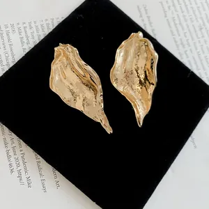 Close-up of textured gold leaf earrings with an irregular wrinkled metal design.
