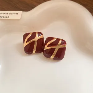 Close-up of square red enamel stud earrings with gold cross pattern on a white tray