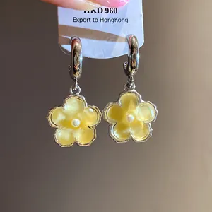 Primo piano di orecchini a fiore in resina gialla con perla centrale e perni in argento.