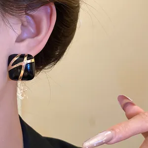 Close-up of elegant square black enamel earrings with gold abstract design