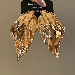Detailed view of gold metallic leaf earrings featuring an irregular pleated texture design.