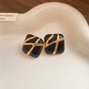 Detailed view of black enamel square stud earrings with elegant gold abstract patterns