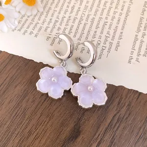 Dettaglio di orecchini a fiore in resina lavanda con perle su un libro vintage