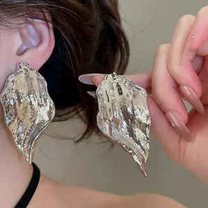 Close-up detail of oversized irregular metallic leaf earrings with textured finish