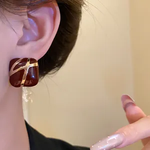 Close-up of square burgundy enamel earstuds with gold accents worn on ear