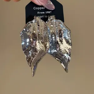 Close-up detail of irregular silver leaf earrings featuring a unique crumpled metallic texture