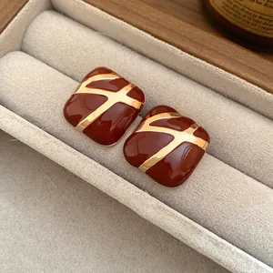 Close-up of elegant burgundy square enamel stud earrings with gold cross pattern