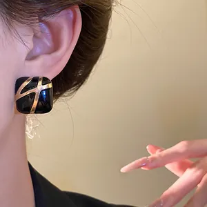 Close-up detail of a stylish square black enamel earring with gold patterns on model