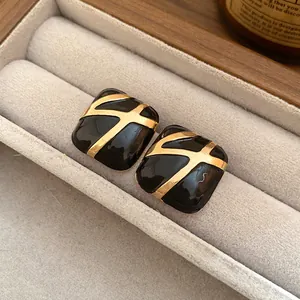 Macro detail showing the black enamel finish and golden lines on square stud earrings