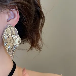 Close-up of a silver irregular leaf-shaped earring with wrinkled metal texture
