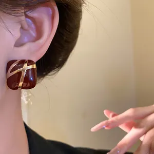 Macro detail of a square burgundy enamel stud earring featuring gold-tone diagonal lines.