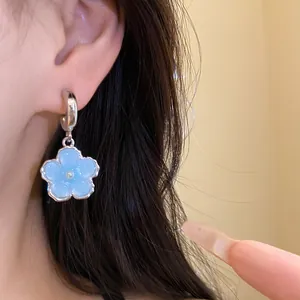 Dettaglio di un orecchino a fiore in resina azzurra con perla indossato da una modella