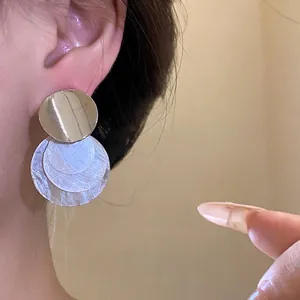 Minimalist silver needle earrings with tiered round shell pendants on model