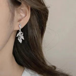 Detailed macro view of silver leaf-shaped drop earrings with zircon inlays on model ear.