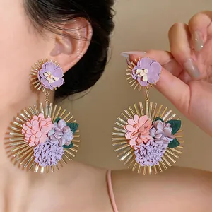 Close-up of oversized floral drop earrings featuring colorful fabric petals and gold