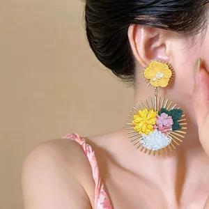 Detail shot of colorful fabric flower earrings with golden sunburst frame on model.