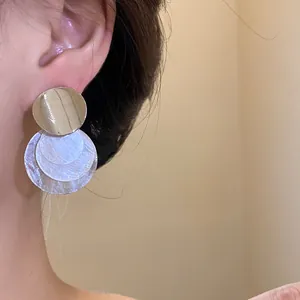 Close-up detail of minimalist silver needle earrings with layered shell circles for women
