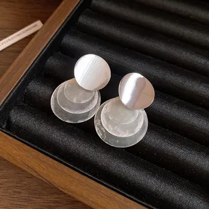 Detailed view of silver needle earrings featuring layered pearlescent shell discs.