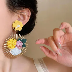 Close-up of bohemian style earrings with colorful fabric flowers and gold sunray frame.