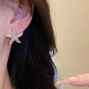 Macro view of a stylish purple starfish stud earring with gold edges worn on ear