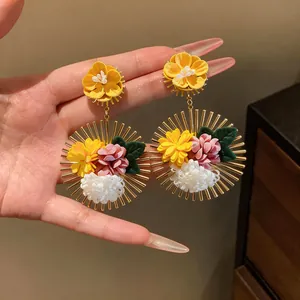 Close-up of vibrant fabric flower earrings with sunburst gold metal frames held in hand
