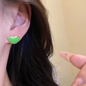 Detailed macro view showing a vibrant green enamel fan-shaped earring on an earlobe.