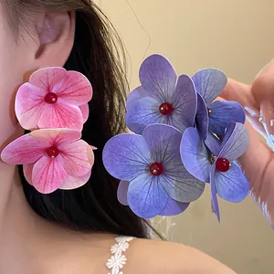 Close-up detail of large fabric hydrangea flower earrings with red bead center.